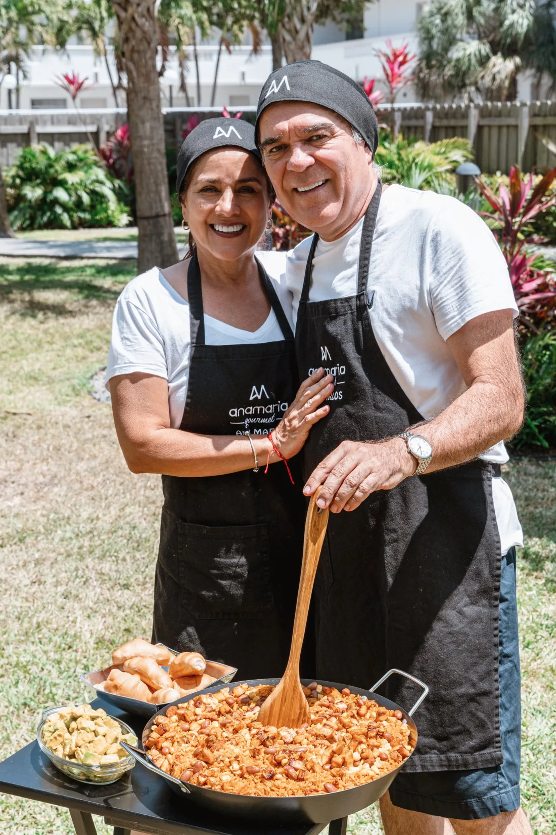 Ana y Juan sonríen abrazados frente a una paellera de Paella Paisa